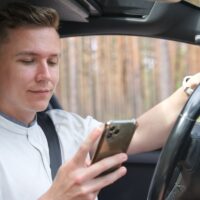 young man driver behind the wheel of a car looks at the screen of the phone