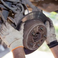 The man's hands remove the worn brake disc from the rear wheel hub. In the garage, a person changes the failed parts on the vehicle. Small business concept, car repair and maintenance service The man's hands remove the worn brake disc from the rear wheel hub. In the garage, a person changes the failed parts on the vehicle. Small business concept, car repair and maintenance service